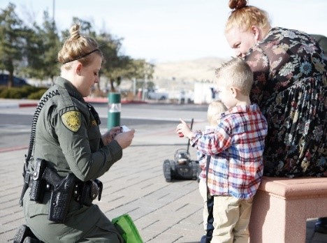 Photo of sheriff deputy giving a sticker to a child wth mom sitting nearby